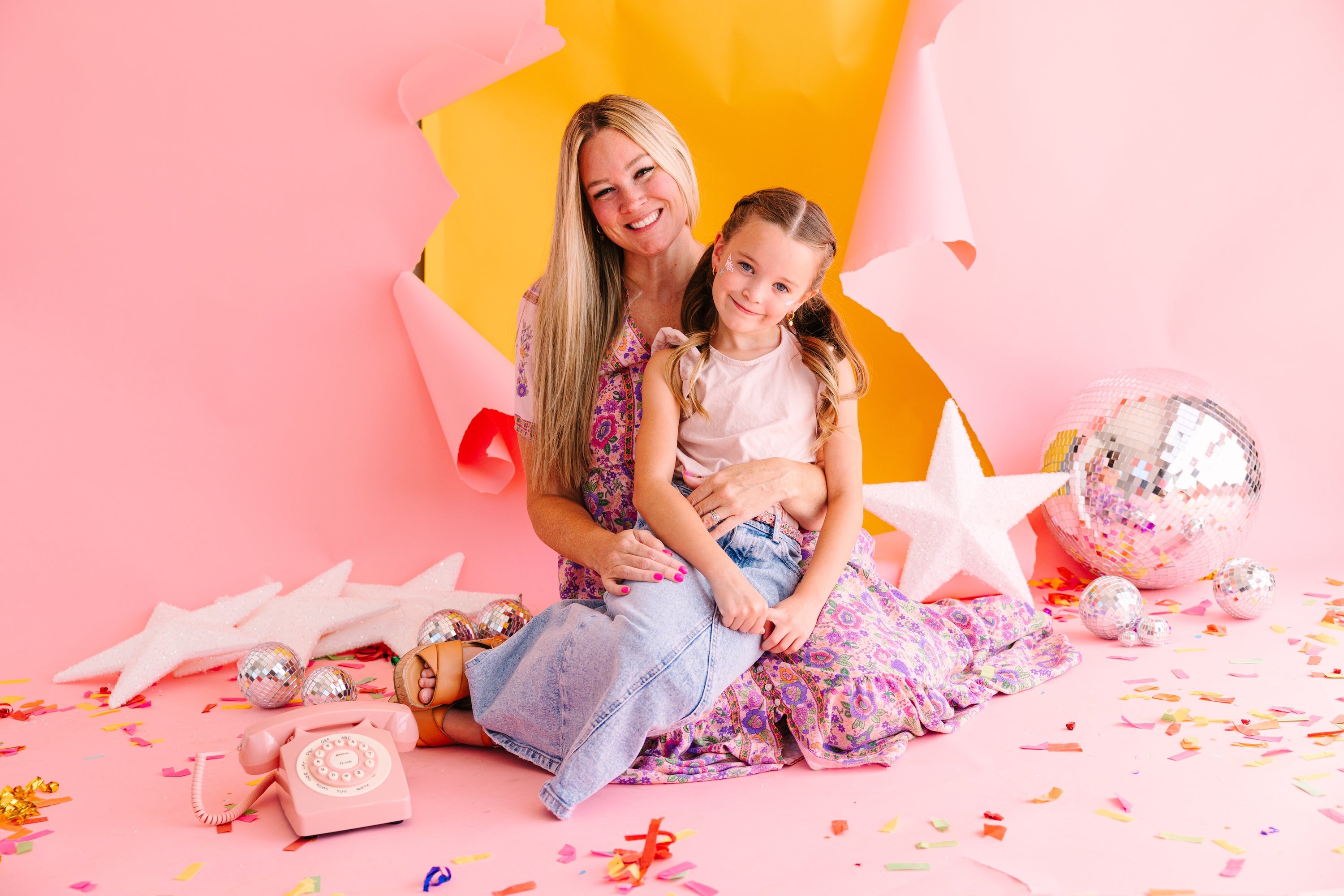 Woman and child sitting on a pink floor with decorative items and balloons.