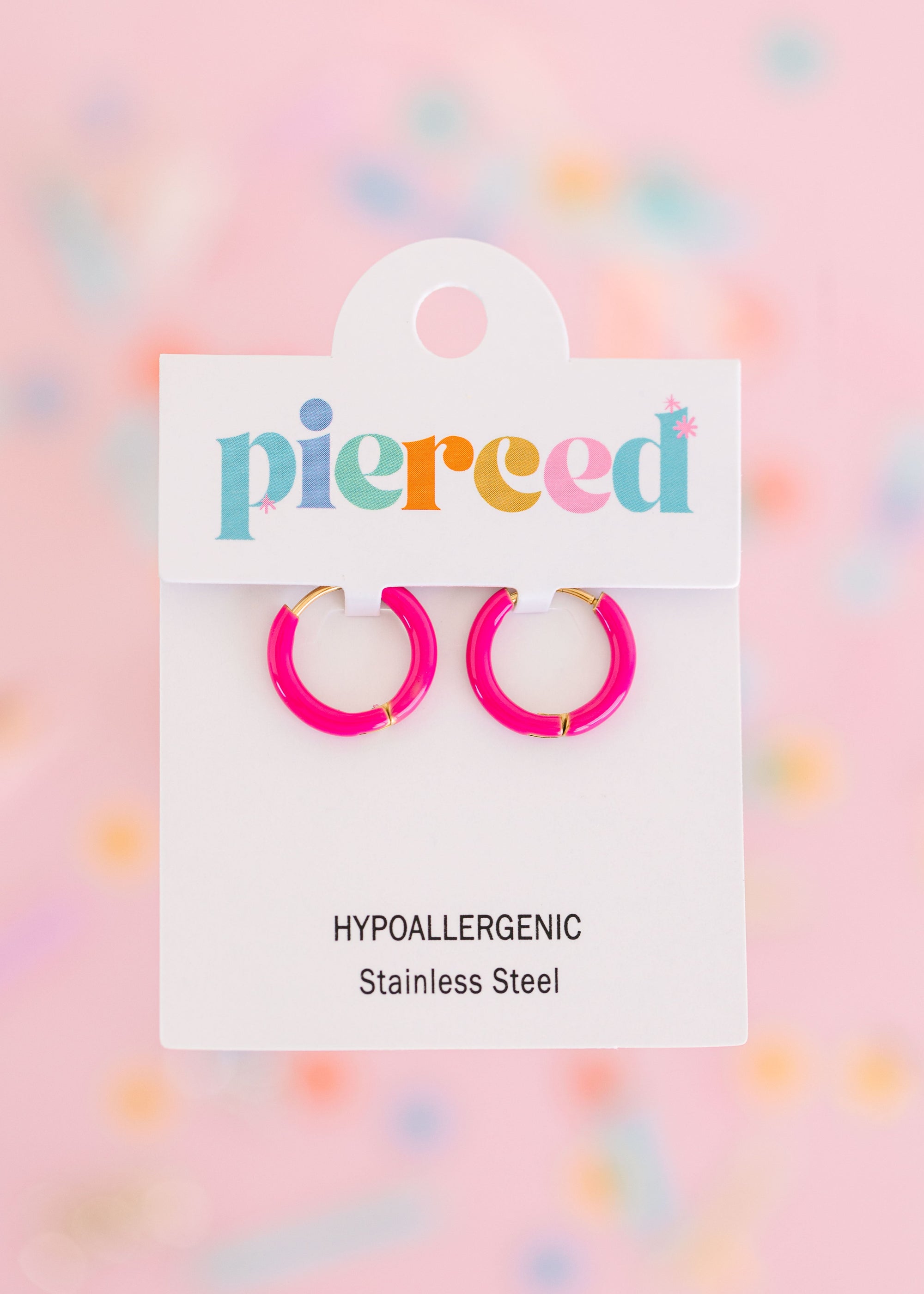 Pink hoop earrings on their packaging card with a colorful blurred background