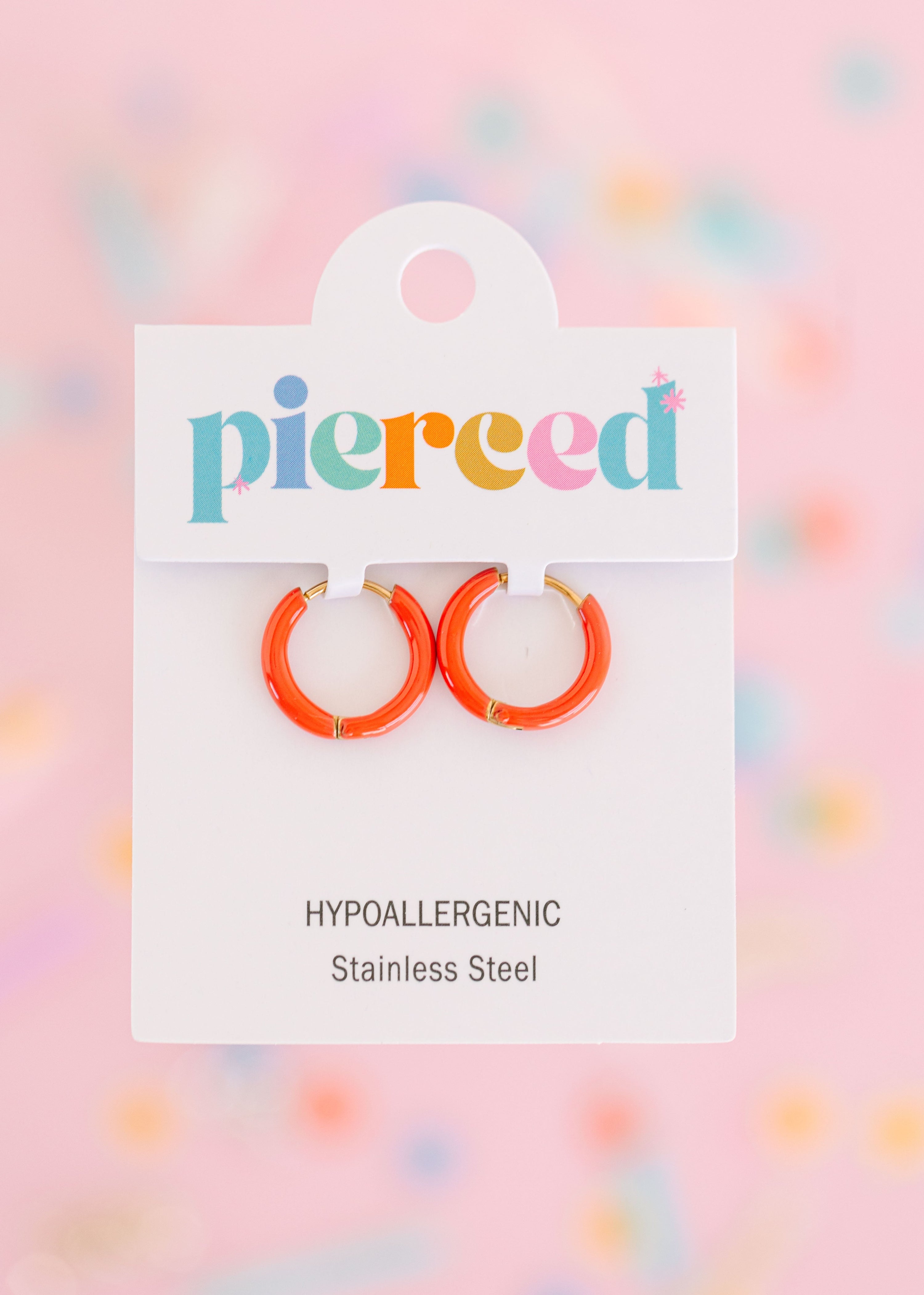 Coral hoop earrings on their packaging card with a colorful blurred background