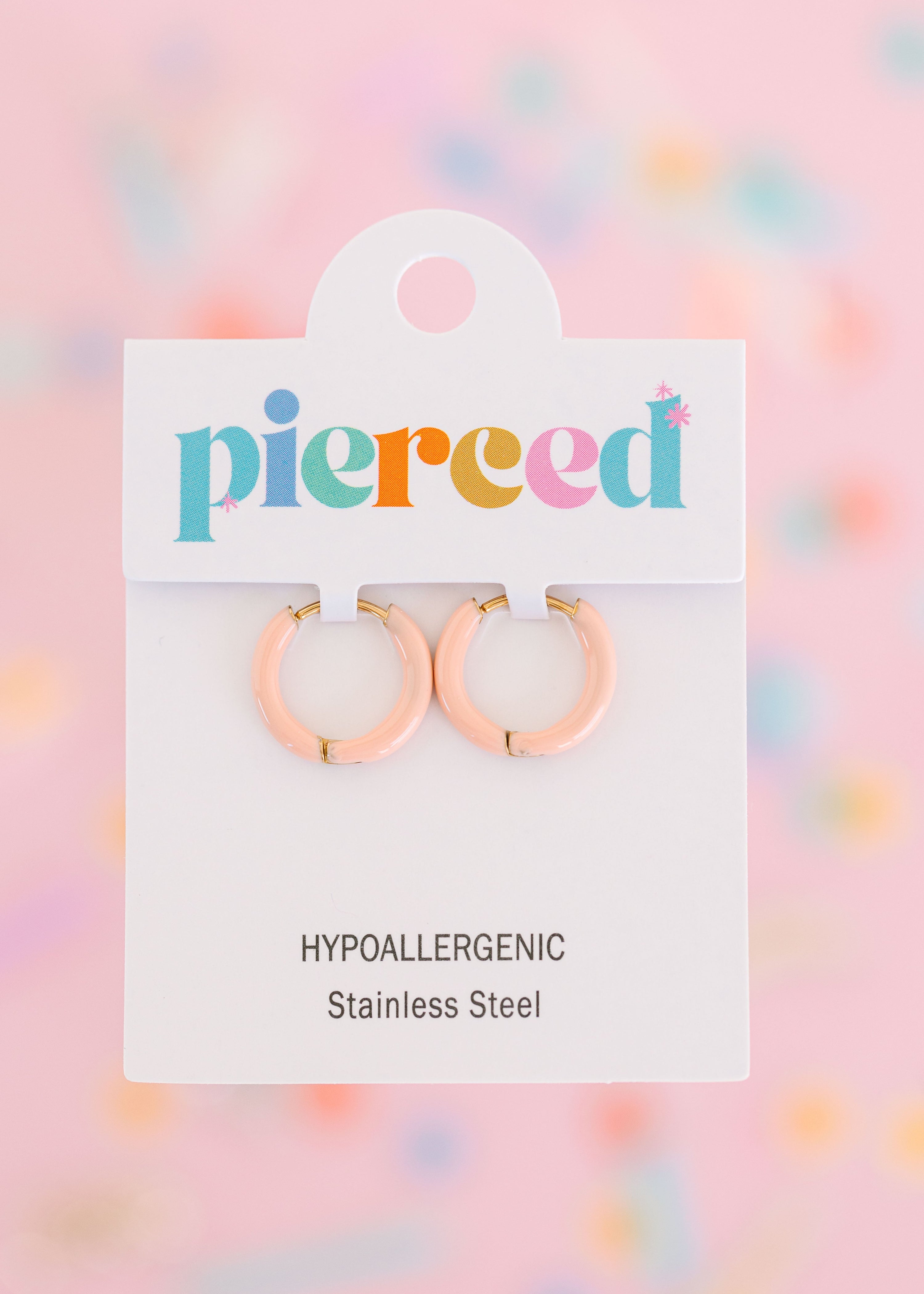 Peach hoop earrings on their packaging card with a colorful blurred background