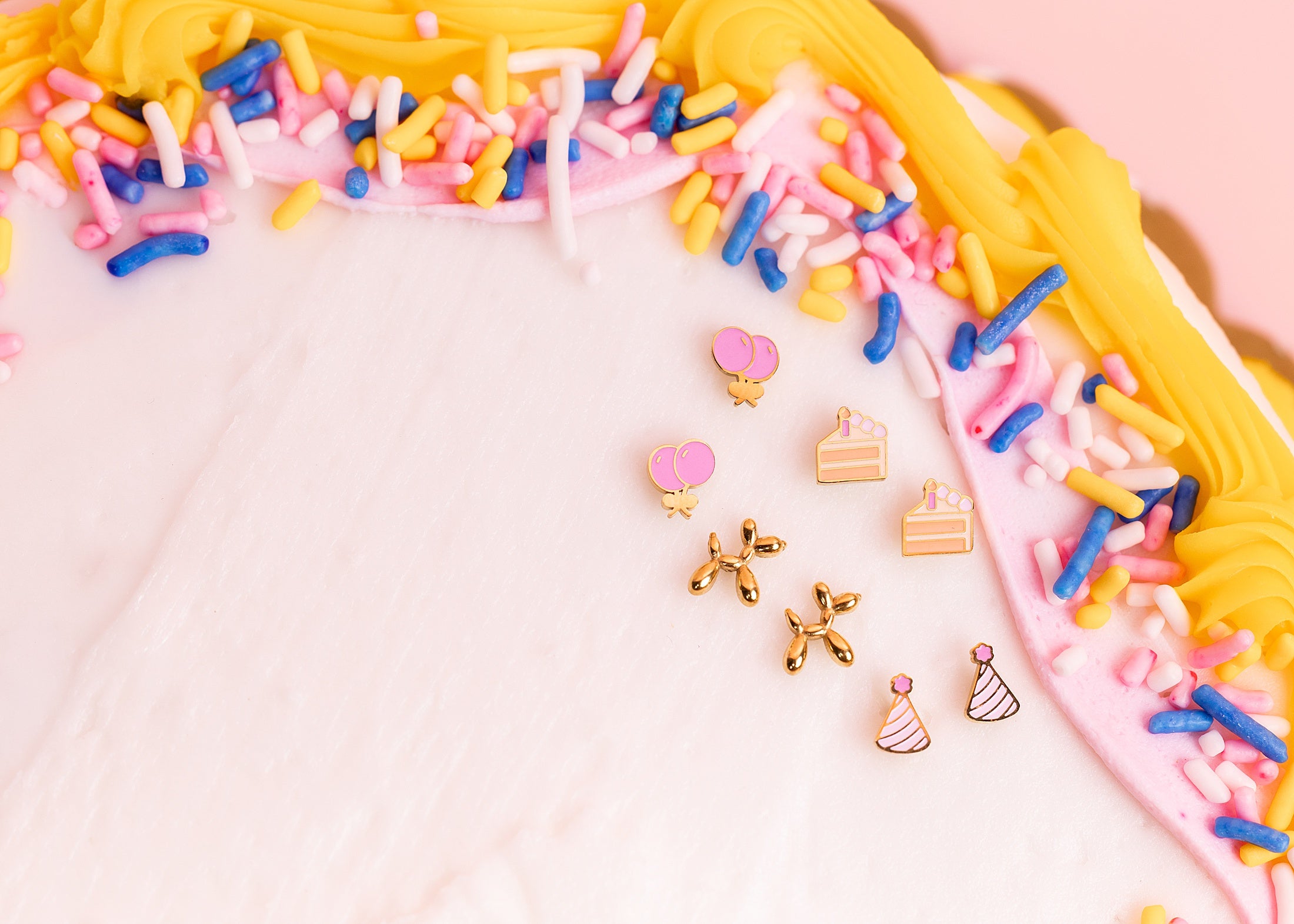 Decorative earrings shaped like small cakes and balloons on a cake with colorful sprinkles.