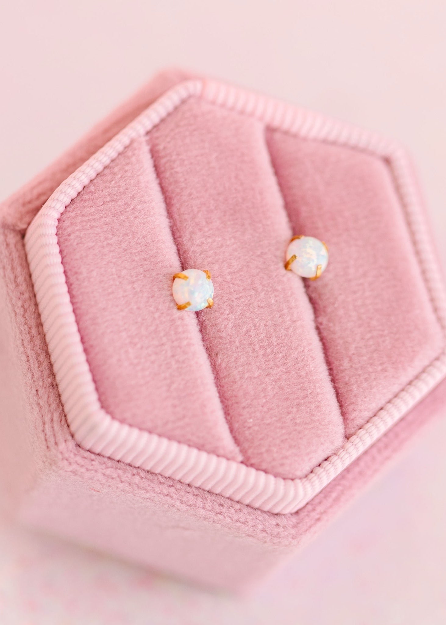 Pair of opal stud earrings on a pink cushioned jewelry box