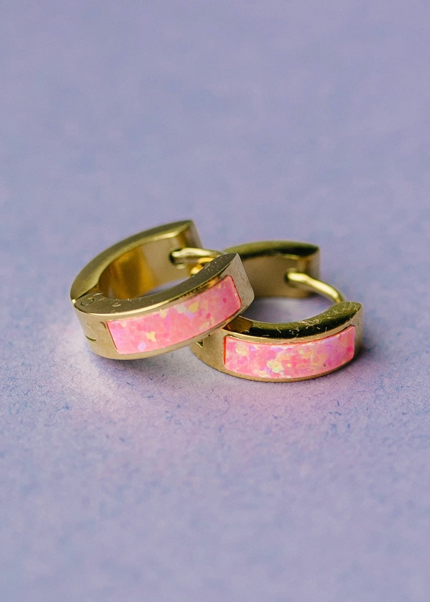 Gold huggies with pink opal inlay on lavender surface