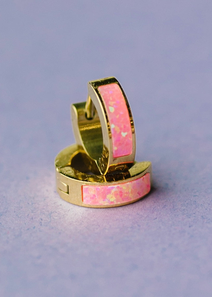 Gold huggie earrings with pink opal detail on purple background