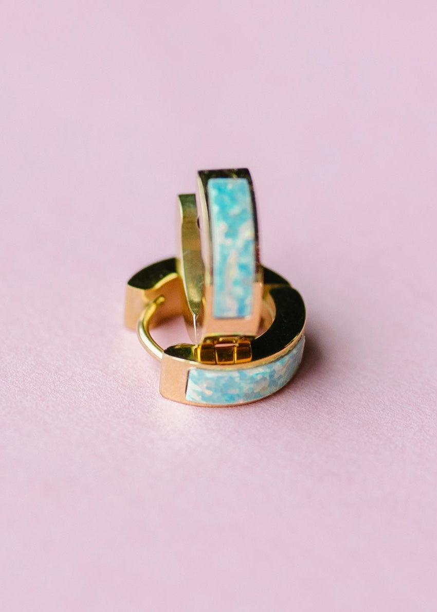 Gold huggies with ocean blue opal on pink background