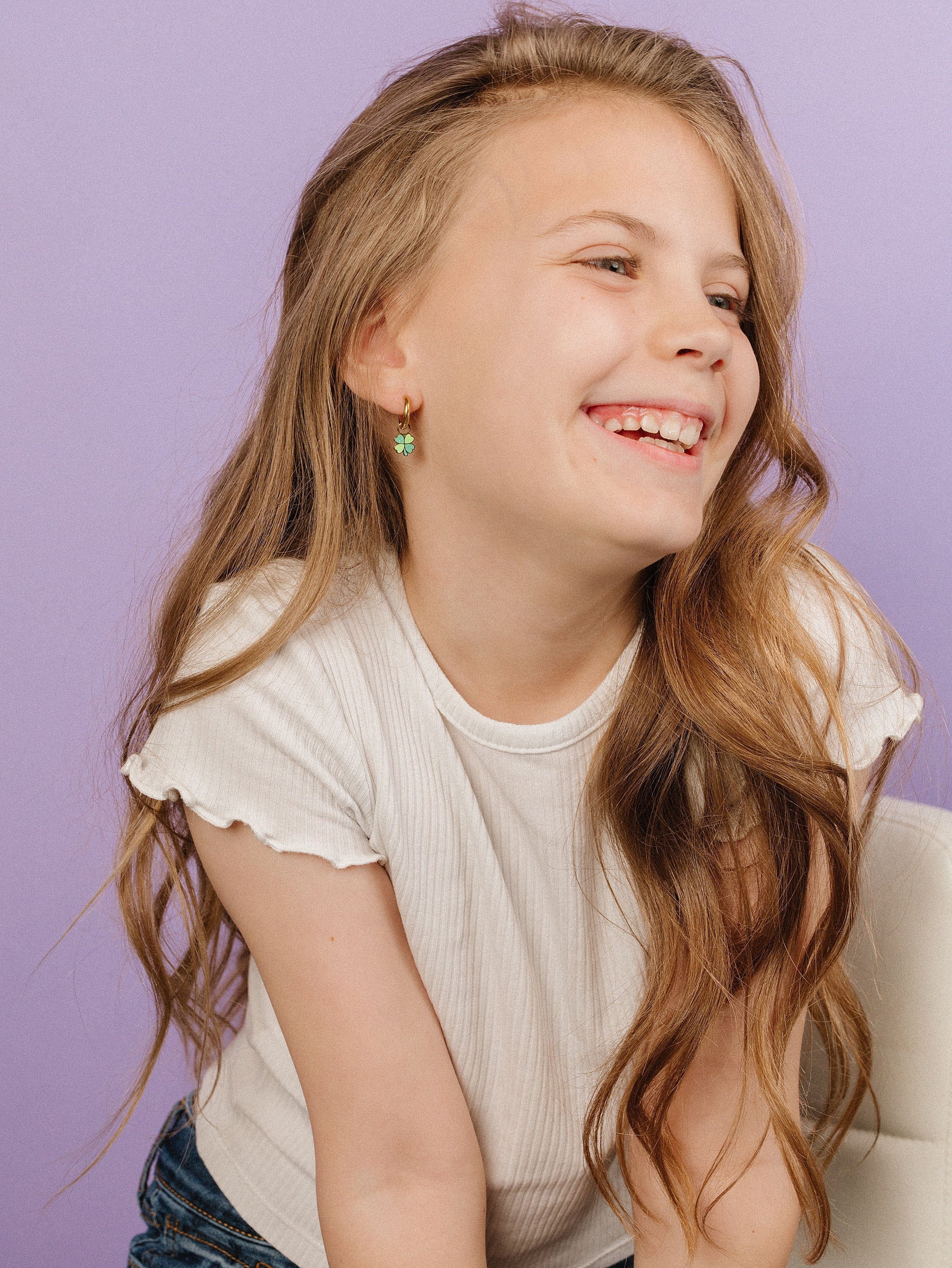 Young girl with long blonde hair wearing a white top against a purple background