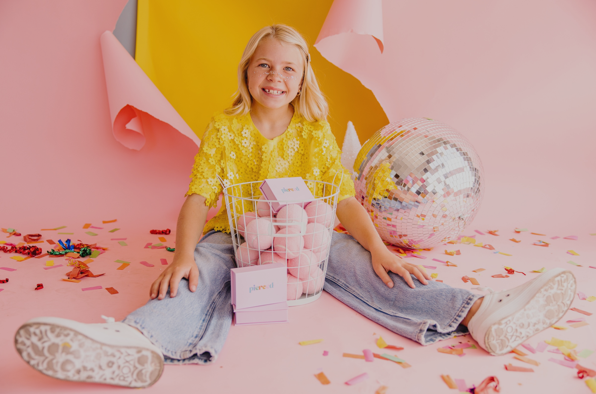 Child in yellow shirt with pink eggs and disco ball on pink floor with confetti